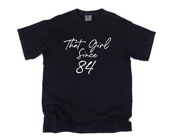 May include: Black t-shirt with white text that reads "That Girl Since 84".