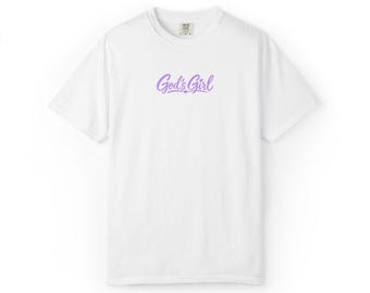 Könnte beinhalten: Ein weißes kurzärmeliges T-Shirt mit dem Text God's Girl in hellvioletter Schreibschrift in der Mitte der Brust. Das T-Shirt hat einen Rundhalsausschnitt und eine Standardpassform, wobei ein kleines Markenetikett am Innenkragen sichtbar ist.