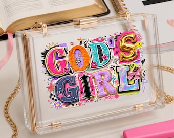 May include: A rectangular clear acrylic box clutch with gold-tone metal hardware and a gold chain strap. The front features a colourful, multi-textured graphic design with the text "GOD'S GIRL" in bold, layered, and decorative lettering.