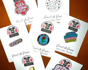 May include: A collection of enamel pins with inspirational messages. The pins feature a variety of designs, including a girl reading a bible, a heart with the words "Start each day with a grateful heart", a plaster with the words "Jesus Heals", a rose with the words "Do no harm but take no shit", a stack of books with the words "Long Story Short", a stack of books with the words "I survived", and a heart with the words "I can do hard things".