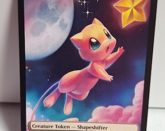 May include: A creature token card featuring a pink, cat-like creature reaching towards a golden star. The card has a night sky background with a large moon and fluffy clouds. Text at the top reads "SHAPESHIFTER". The bottom text reads "Creature Token - Shapeshifter".