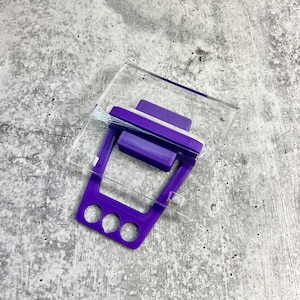 May include: A purple plastic stamp with a clear acrylic base. The stamp has three holes in the bottom and a handle on the top.