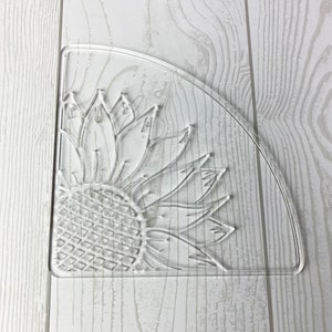 May include: Clear plastic corner shelf with a sunflower design. The shelf is shaped like a quarter circle and has a raised sunflower design.