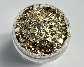 May include: A clear, round container filled with gold glitter. The glitter particles vary in size and shape, reflecting light with a shimmering effect. The glitter appears to be a mix of gold and silver tones, creating a sparkling appearance.