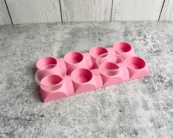 Puede incluir: Organizador de plástico rosa con ocho compartimentos redondos para guardar objetos pequeños. El organizador tiene un acabado liso y mate.