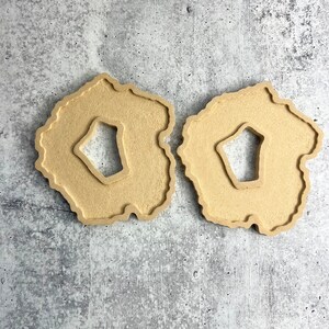May include: Two wooden coasters with a unique agate design. The coasters are beige and have a cutout in the center.