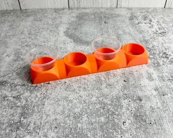 Puede incluir: Portavasos de plástico naranja con cuatro vasos de plástico transparentes. El portavasos está diseñado para contener recipientes pequeños.