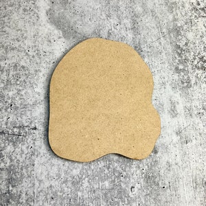 May include: A blank, brown, wooden cutout in the shape of a ghost. The cutout is on a gray, textured background.