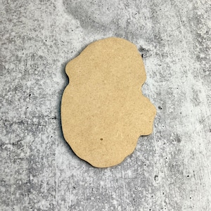 May include: A brown wooden cutout of a human head shape, with a slightly irregular outline. The cutout is on a gray textured background.
