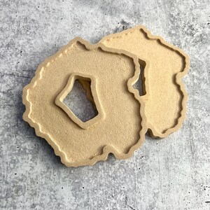 May include: Two beige resin coasters shaped like agate slices with a cutout in the center.