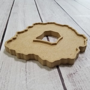 May include: A light brown wooden coaster with an irregular, agate-like shape and a smaller, circular cutout in the center.