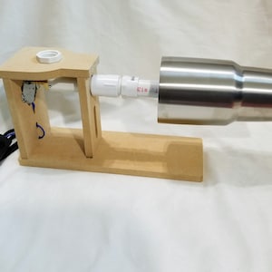 May include: A wooden tumbler turner with a stainless steel tumbler attached. The turner has a white PVC pipe and a power cord with a black switch. The text "#13" is visible on the pipe.