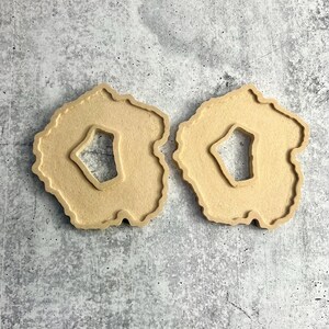 May include: Two beige wooden coasters shaped like agate slices with a cutout in the center.