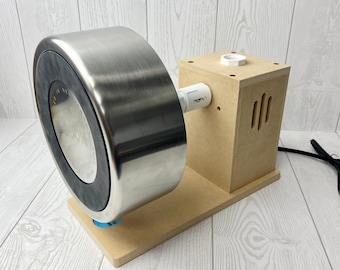 May include: A stainless steel tumbler turner with a wooden base and support. The tumbler is held in place by a black rubber ring. The wooden base has a square support with ventilation slots and a white PVC pipe.