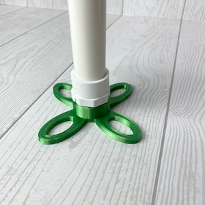 Puede incluir: Una base verde impresa en 3D con cuatro brazos, dise&ntilde;ada para sujetar un tubo de PVC blanco. La base tiene un accesorio de tubo de PVC blanco.