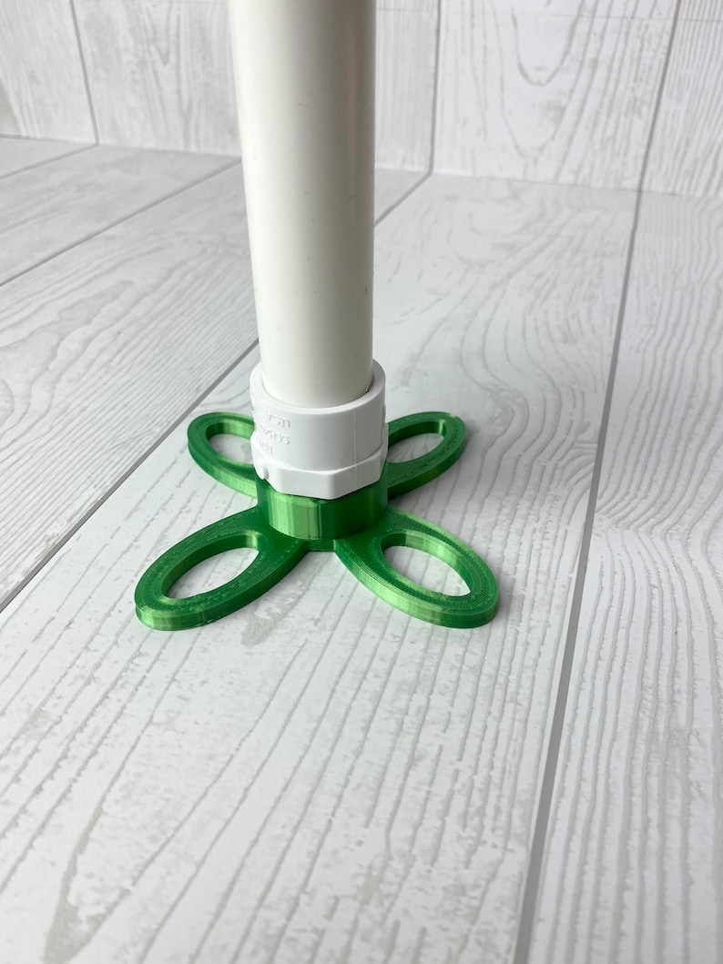 Puede incluir: Una base verde impresa en 3D con cuatro brazos, dise&ntilde;ada para sujetar un tubo de PVC blanco. La base tiene un accesorio de tubo de PVC blanco.