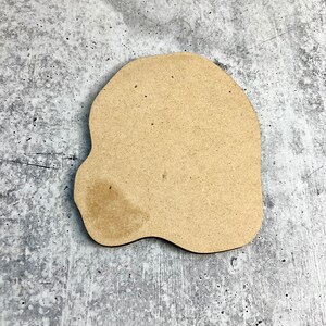 May include: A light brown, irregularly shaped wooden cutout, resembling a cloud or a blob, on a gray textured background.