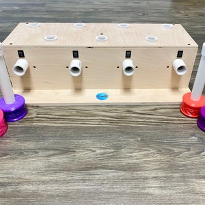 May include: A wooden tumbler turner with eight white PVC pipe arms and colored bases. The turner has a light wood finish and a blue sticker. The bases are pink, purple, and orange.