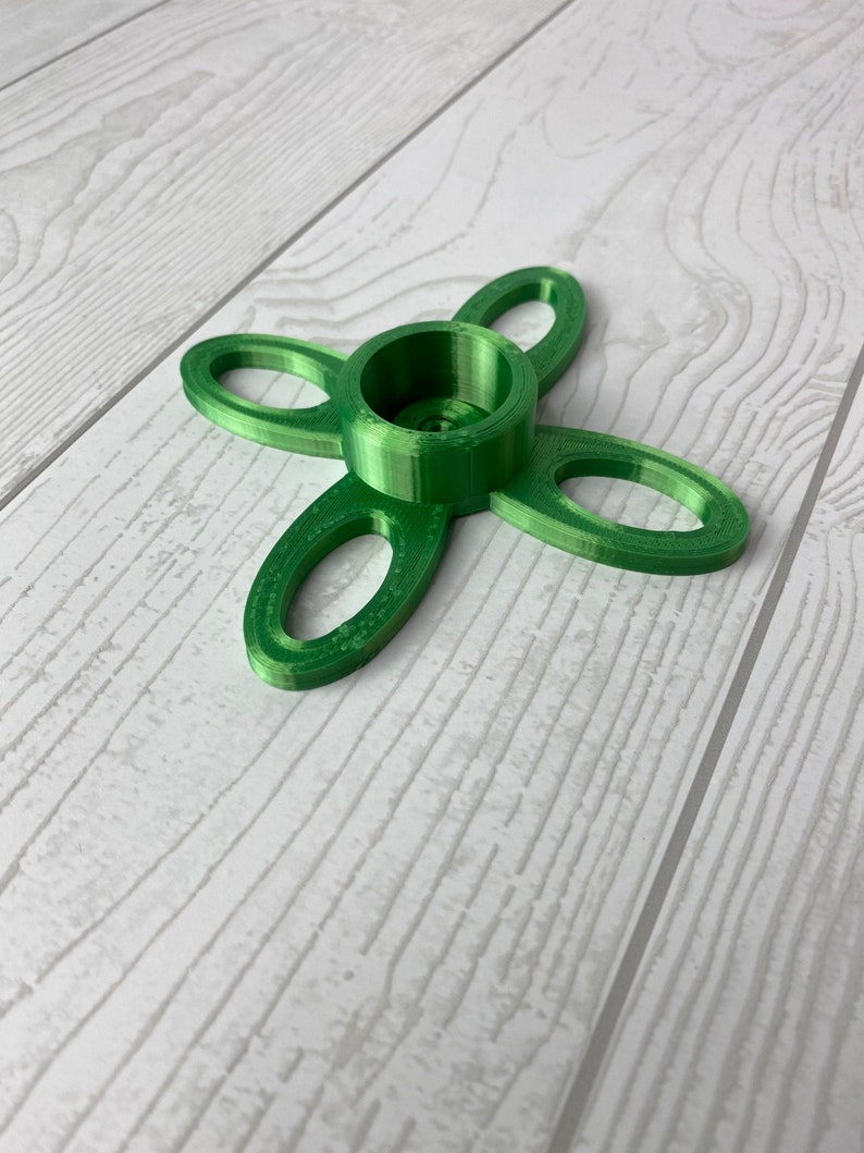 Puede incluir: Un portavelas verde impreso en 3D con cuatro brazos en forma de bucles. El portavelas tiene una abertura circular central para una vela.