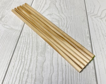 Puede incluir: Un paquete de diez clavijas de madera natural, de aproximadamente 30 cm de largo, de color marrón claro. Las clavijas están apiladas cuidadosamente sobre una superficie de madera blanca.