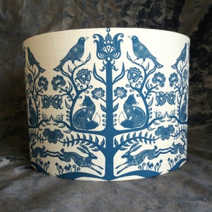 Puede incluir: Una pantalla de lámpara azul y blanca con un diseño caprichoso que presenta pájaros, zorros y conejos en un entorno de bosque.