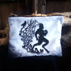 May include: A white zippered pouch featuring a black silhouette of a goat-like creature running through a forest with a crow perched on a branch. The background is a distressed white with black accents.