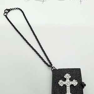 May include: Black chain necklace with a black glitter book charm featuring a silver rhinestone cross. The charm has a small silver clasp.