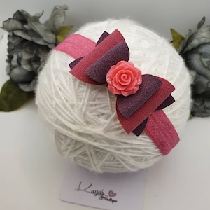 May include: A pink and purple layered bow with a pink flower in the centre, attached to a pink elastic headband.
