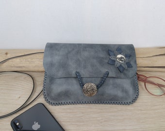 May include: A gray suede crossbody bag with a decorative flower and a metal button closure. The bag has a long strap and is made of a soft, textured material.