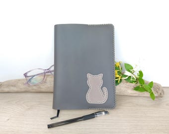 May include: Gray leather journal with a stitched edge and a light gray cat applique. A black pen and a pair of purple-framed glasses are next to the journal. The journal has a black ribbon bookmark.