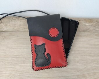 May include: A black and red leather phone case with a black cat silhouette and a red circle. The case has a strap for carrying.