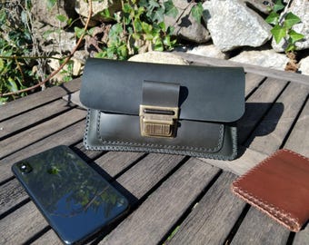 May include: A black leather purse with a brass clasp and a stitched design. The purse is sitting on a wooden surface with a brown leather wallet and a black smartphone.