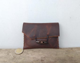 May include: A brown leather wallet with a wooden button closure. The wallet has a distressed look and is stitched around the edges.