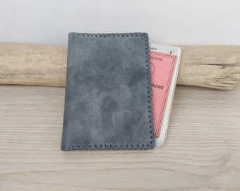 May include: A gray leather passport holder with a stitched edge. The holder is empty and is sitting on a wooden surface.
