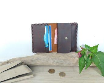 May include: A dark brown leather wallet featuring visible stitched edges, a snap button closure, and multiple interior slots containing blue and white cards. The wallet is constructed with a smooth finish and displays a rectangular shape with rounded corners.