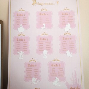May include: A pink wedding seating chart with gold accents and a fairytale theme. The chart features eight tables with guest names, decorative crowns, and Disney character cutouts. The text "Be our guest..." is also visible.