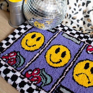 Puede incluir: Una alfombra morada con un borde a cuadros y tres caras sonrientes amarillas. La alfombra est&aacute; sobre un suelo de madera con una bola de discoteca y una l&aacute;mpara de lava en el fondo.
