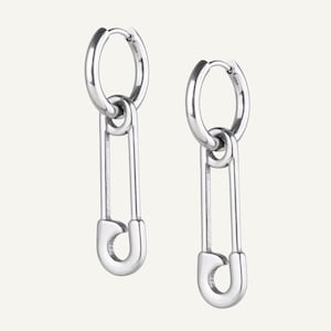 Op de afbeelding: Een paar zilverkleurige oorringen met een veiligheidsspeldontwerp. De oorbellen zijn gemaakt van glanzend metaal en hangen aan een cirkelvormige ring. De veiligheidsspeld heeft een klassiek ontwerp.