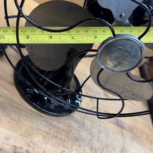 May include: Vintage black electric fan with a silver fan blade and a black cage. The fan's blade span measures approximately 8 inches. The fan has a round emblem with the text "Polaris Electric".