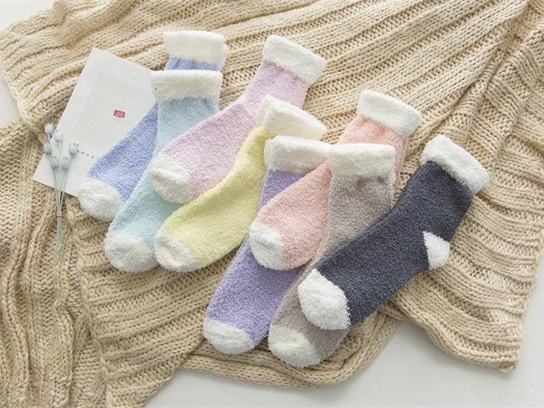 May include: A set of eight fuzzy socks in various pastel colors, including light blue, pink, lavender, and yellow. The socks are made of a soft, fluffy material and have a white cuff.