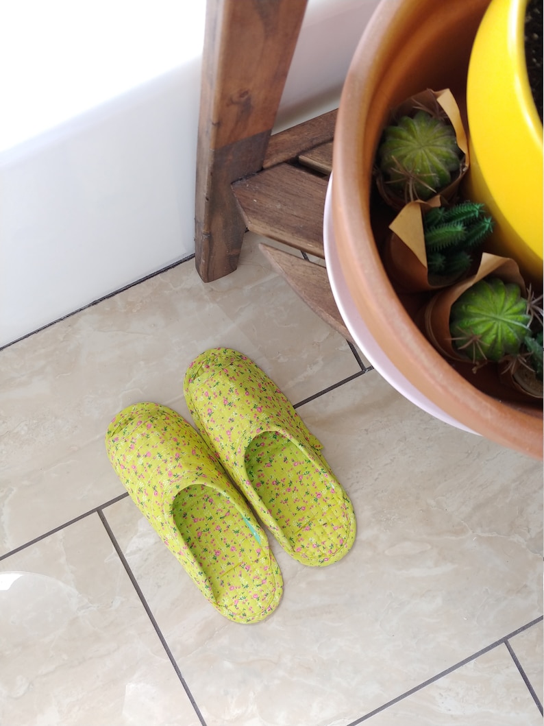 May include: A pair of green floral print slippers with pink flowers. The slippers are on a tiled floor.