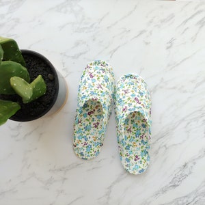 May include: A pair of white floral print slippers with blue and purple flowers. The slippers are on a white marble surface.