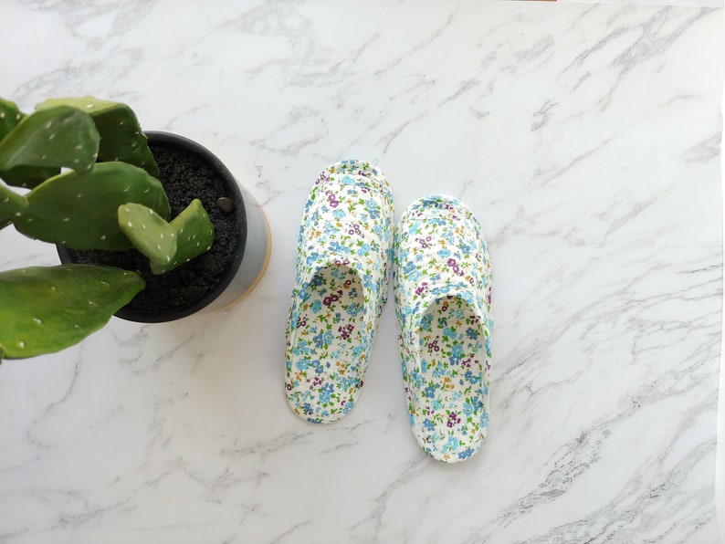 May include: A pair of white floral print slippers with blue and purple flowers. The slippers are on a white marble surface.