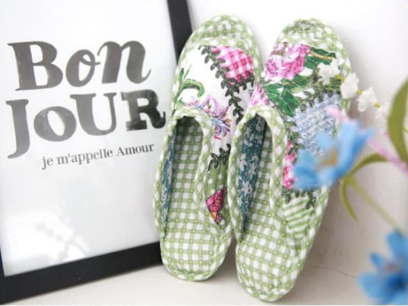 K&ouml;nnte beinhalten: Ein Paar gr&uuml;ne und wei&szlig;e karierte Hausschuhe mit Blumenstickerei. Die Hausschuhe haben ein Gingham-Muster und zeigen eine Vielzahl von Blumen in Rosa, Blau und Gr&uuml;n.