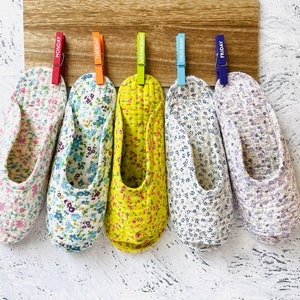 May include: Five pairs of floral patterned slippers hanging on a wooden board with clothespins labeled Monday through Friday.