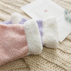 May include: A pair of fuzzy socks with pink and purple stripes. The socks are made of a soft, fluffy material and have a white cuff.