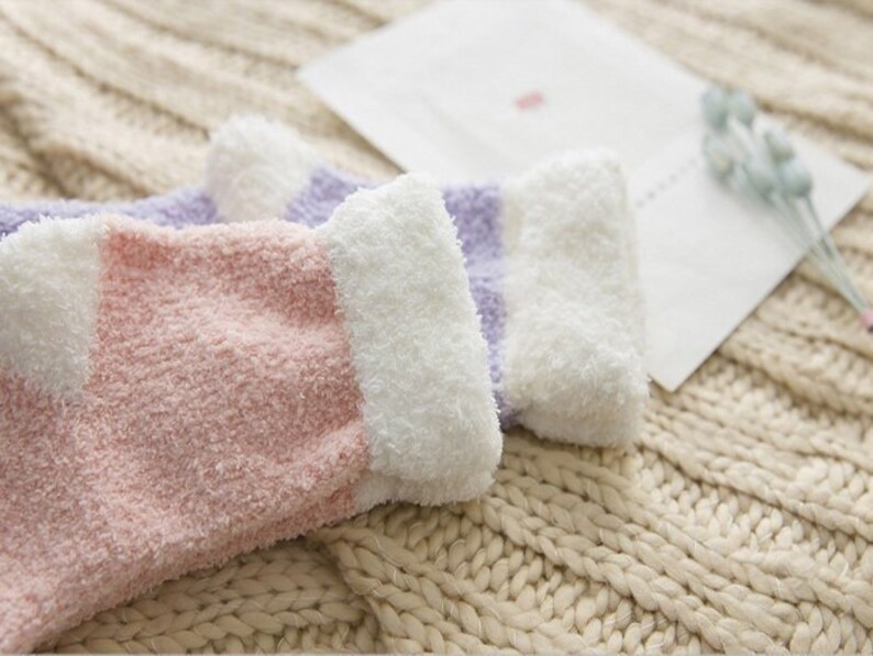 May include: A pair of fuzzy socks with pink and purple stripes. The socks are made of a soft, fluffy material and have a white cuff.