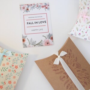 May include: Three pillow boxes with different floral patterns and ribbons. The boxes are white with pink flowers, beige with orange flowers, and brown with a brown floral design. The boxes are tied with ribbons in different colors. The boxes are perfect for packaging small gifts or favors.