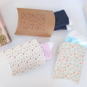 May include: Four gift boxes with different patterns. Two boxes are brown with white floral designs, one is brown with a white pineapple design, and one is white with a pink floral design. The boxes are filled with socks.
