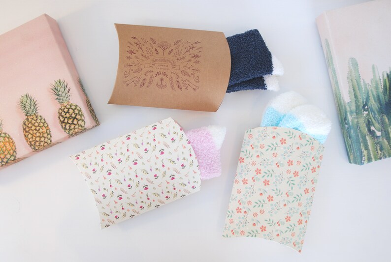 May include: Four gift boxes with different patterns. Two boxes are brown with white floral designs, one is brown with a white pineapple design, and one is white with a pink floral design. The boxes are filled with socks.